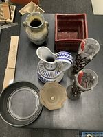 Photo showing seven assorted items including ceramic, glass, and metal vases, pots and bowls on a grey surface.