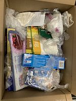 Top-down view of open cardboard box filled with kitchen disposable items including Ziploc bags box, coffee filters, and aluminum foil roll with packaging.