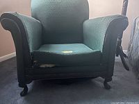 Side angled closeup of armchair showing fabric damage on armrest, sturdy dark wood frame and legs.