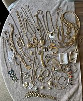 Multiple gold-tone necklaces, bracelets, rings and brooches arranged on towel