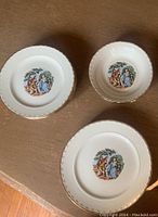 Three Crooksville China pieces: one bowl and two plates, showing detailed rural scene with people and trees, gold trim