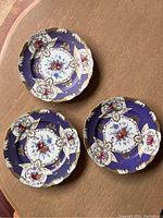 Three purple decorative plates displaying floral patterns and gold scroll design on a wooden table.