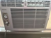 Close-up photo of Frigidaire window air conditioner front panel showing grille vents and control knobs for temperature and fan.