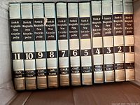 Spine view of volumes 1 through 11 of the Funk & Wagnalls "New" Encyclopedia full set, showing volume numbers and partial subject indexing.