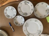 Set of plates and bowls displaying floral pattern and gold trim on beige surface, includes various sizes.
