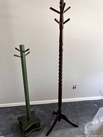 Green and brown wooden coat racks side by side on floor, showing overall height and base shapes.