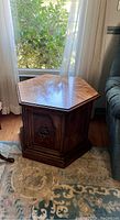 Hexagonal wooden end table positioned next to a window, showing its shape and wood finish.