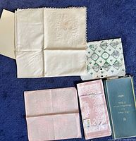 Photo showing off-white tablecloth with lace edging and slight yellow stain on one corner, along with pink napkins and original packaging.