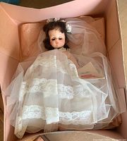 Bride Madame Alexander Doll laying in original box wearing full lace wedding dress and long veil with flower crown. Original tag visible.