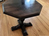 Full view of octagon wooden table showing top and pedestal base with carved details.