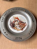 Pewter plate with central colored illustration of Revolutionary War battle and raised text on rim