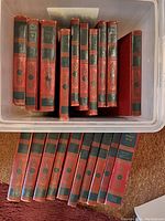 Photo showing multiple hardcover volumes of The World Book Encyclopedia with red and black spines in a plastic container.