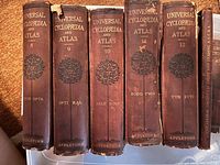 Spine view showing volumes 8 through 12 of Appleton's Universal Cyclopedia and Atlas. Each volume has a brown hardcover with gold text and an embossed tree emblem. Visible weathering and edge wear.