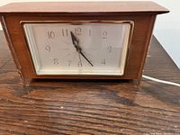 Front view of the vintage wooden mantel clock with clear rectangular face showing the time, placed on a wooden table.