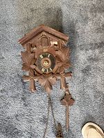 Front view of vintage Linatz cuckoo clock showing wooden housing, detailed leaf carvings, clock face with Roman numerals, and pendulum.