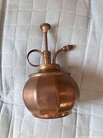 Front angled view of vintage solid brass perfume atomizer showing bulbous body, pump, and nozzle