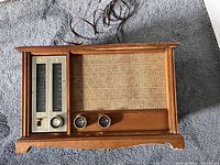 Front view of the vintage radio showing the wooden cabinet, woven speaker fabric, tuning display, and control knobs.