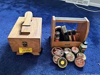 Two wooden shoe shine items on blue carpet: shoe server box with handle and polish caddie holding brushes and cans of Kiwi polish.