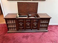 Full front view of closed wooden stereo console with three-section front and carved side panels