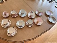 All ten vintage tea cup and matching saucer sets plus two additional plates shown on a table with visible floral and patterned designs.