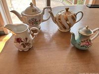 Top view of three decorative small teapots and a matching creamer displayed on a table near a window with natural light.
