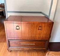 Front view of the wooden vintage TV cabinet with square pattern on top, two doors with metal handles, and a large bottom drawer with handle intact.