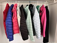 Thirteen women's winter jackets and vests hung on a rod.