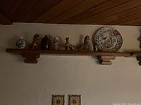 Wall mounted wooden shelf holding small decorative ceramic figurines and plates including a floral patterned plate and animal shaped figurines.