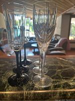 Six champagne flutes arranged on a marble surface, showing both clear and black stemmed glasses with decorative cut glass bowls.