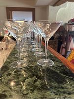 Side angle view of the 8 clear martini glasses lined up on a green marble surface showing their uniform shape and size.