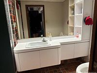 Front angle of white floating vanity showing built-in sink, faucet, large mirror, and shelving unit on right