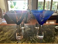 Four martini glasses in blue and purple colors with clear thick stems shown from above on a counter.