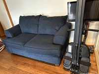 Blue corduroy loveseat couch side view showing two seat cushions, two back cushions, and rounded armrests on a wooden floor with exercise equipment nearby.