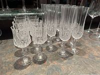 Set of 11 champagne glasses and 8 wine glasses arranged closely on countertop, showing clear crystal with intricate cut details.