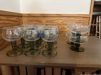 Ten glasses grouped together showing painted floral designs on most and clear glasses on two.