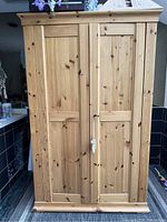 Front view of wooden armoire with closed doors showing natural wood grain and key lock on right door.