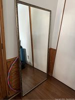 Large rectangular mirror leaning against wall showing metallic frame and clear reflective surface
