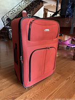 Side angle view of red Delsey rolling suitcase showing two zippered front pockets and retractable handle.