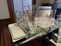 Overview of all 8 barware items placed on a green marble tabletop showing trays, pitchers, bowl, ice bucket, vase, decanter.
