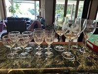 View of all 12 wine glasses in the set, showing four tall etched glasses, four shorter etched glasses, and four small cut-glass glasses on a marble countertop.