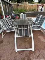 View from one end of the outdoor patio table showing glass top and two striped chairs on either side.
