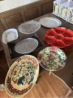 Top-down view of all 8 serving platters on wooden table showing variety in shapes, materials, and designs