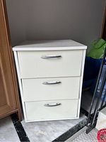 Front view of white 3-drawer storage cabinet with silver curved handles, shows some marks on drawers.
