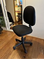 Front angle view of the black fabric swivel office chair with no armrests showing seat, backrest, base with caster wheels.
