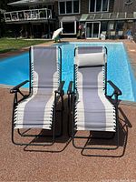 Front-facing photo showing two zero gravity lounge chairs by a poolside with fabric slings and removable pillows.