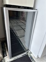 Closed wine fridge with transparent glass door showing silver frame and black sides.