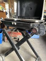 Side view of portable grill showing foldable legs, one side tray, and control knob.