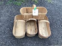 Four wooden berry baskets on gravel surface, three shallow oval baskets with slatted sides and one double-compartment basket with handle.