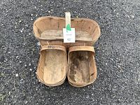 Photo of three wooden berry baskets placed on gravel. One large oval basket with a central handle in the back and two smaller rectangular baskets in front.