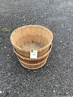 Two stacked wooden bushel baskets placed on gravel ground showing natural wood and metal band reinforcement
